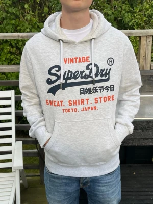 Superdry hoodie - Använd men fortfarande i fint skick Fotfarande mjuk o skön i tyget Storlek L Modellen är 180cm och 66kg Någon mindre fläck som ska gå bort i tvätten