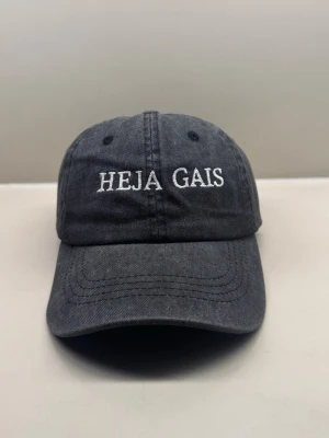 HEJA GAIS-keps - Vintage washed dad cap - Svart vintage washed-keps med broderad HEJA GAIS-text framtill.  Justerbar baktill och passar både dam & herr. Snygg till match, vardag eller som supporterkeps.  Fint skick  