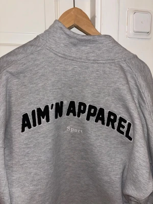 Grå zip hoodie från AIM'N APPAREL - Snygg grå zip hoodie från AIM'N APPAREL med svart broderad logga på ryggen och texten 'Sport' under. Hoodien har hög krage, dragkedja framtill och avslappnad passform. Perfekt till chill eller träning. snygg jacka, bra att ha när man tränar ❤️nypris 800kr. ❤️