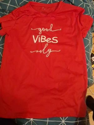 Röd t-shirt med texttryck - Säljer en röd t-shirt med vit text 'good vibes only' på framsidan. T-shirten har korta ärmar och en klassisk rund halsringning. Perfekt för dig som vill ha en chill och positiv stil.