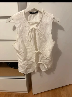 Vit brodera ärmlös topp med knyt - Supersöt vit topp från Bik Bok med broderade detaljer och tre knyt framtill. 