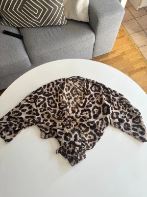 Leopardmönstrad blus med knyt - Snygg blus med leopardmönster i beige, brunt och svart. Modellen har v-ringning och knyt framtill, samt långa ärmar. Tunt och lätt material som ger en luftig känsla. Perfekt för dig som vill sticka ut med ett djurmönster.