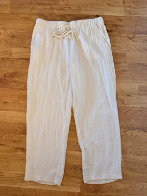 Vita linnebyxor med dragsko - Säljer ett par luftiga vita linnebyxor med resår i midjan och dragsko. Byxorna har raka ben och sidfickor, perfekta för en avslappnad och stilren look. Materialet är tunt och svalt linne som passar bra till sommaren.