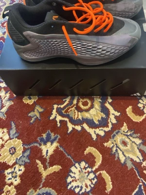 Gråa anothony Edwards 1 j low med orange snören. Adidas - Säljer ett par AE1 i metralic grey med grå och silvriga detaljer samt orange snören. Skorna är bra för bandet och väldigt snygga med meshpaneler på sidorna och en låg siluett. Perfekta för dig som vill bli bra på planen och lätta.