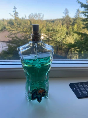 Grön parfymflaska i form av torso - Unik parfymflaska med grön vätska, formad som en manlig torso. Flaskan har detaljerade former och en dekorativ stjärna i blått, orange och svart vid basen. Perfekt för dig som gillar snygg design på parfymflaskor. 125 ml ca 100-110 kvar ny pris 1600