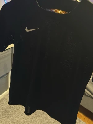 Svart träningströja från Nike - Säljer en svart träningströja från Nike med klassisk vit swoosh-logga på bröstet. Tröjan har rund halsringning och korta ärmar, perfekt för gymmet eller löpning. Materialet är lätt och andas bra.