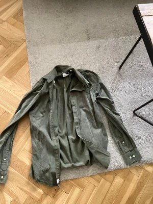 Grön manchester skjorta från Casual Friday - Snygg grön skjorta i mjuk manchester från Casual Friday. Skjortan har klassisk krage, långa ärmar med knappar vid manschetterna och en bröstficka. Perfekt för en avslappnad men stilren look.