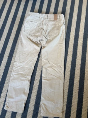 Beiga raka jeans Hansen och Jacob 30/32 - Säljer ett par beiga jeans med rak passform och klassisk femficksdesign. Jeansen har bälteshällor och en patch vid linningen bak. Perfekta för en clean och avslappnad stil.