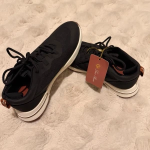 Loro Piana Tennis Walk Sneakers - Snygga svarta sneakers med vit tjock sula och bruna detaljer på hälen. Ovandelen är i mesh och syntetmaterial för en sportig look. Klassisk snörning och stilren design som passar till det mesta.