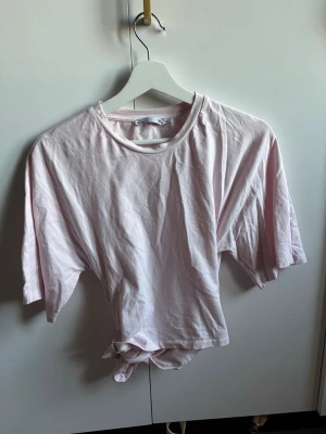 Ljusrosa topp med knyt - Säljer en ljusrosa croppad topp i mjuk bomull med korta ärmar och knyt i midjan. Perfekt för dig som gillar en avslappnad men ändå trendig stil. Toppen har enkel rund halsringning och är superenkel att matcha med jeans eller kjol.