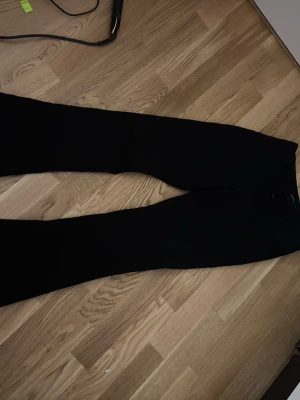 Svarta utsvängda byxor Gina Tricot - Svarta utsvängda byxor från Gina Tricot i stretchigt material. Byxorna har hög midja och en smal passform upptill som blir vidare nedtill. Perfekta för en trendig och bekväm look.