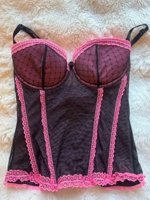 Svart/rosa korsett med spets  - Säljer en ganska unik och snygg svart korsett med rosa detaljer och spetskanter från h&m. Kuporna är vadderade och har ett rutmönster med små prickar. Axelbanden är justerbara och materialet är genomskinligt mesh. Vid frågor är det bara att höra av sig! Storlek 40, men funkar bra för mig som vanligtvis är 34/36!💕💕