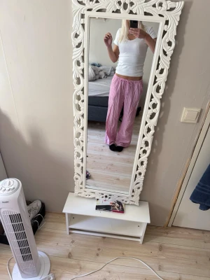 Rosa randiga pyjamasbyxor - Säljer ett par rosa pyjamasbyxor med vita vertikala ränder. Byxorna har en avslappnad passform och resår i midjan för extra komfort. Perfekta för mysiga hemmakvällar eller lata morgnar.