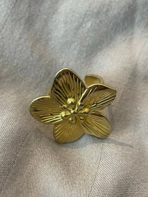 Guldfärgad blomring  - Snygg guldfärgad ring i form av en stor blomma med detaljerade blad och små kulor i mitten. Ringen är justerbar och har en glansig finish som gör den till ett statement-smycke. Perfekt för dig som gillar unika accessoarer med blommig design. Stainless steal. Justerbar