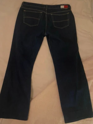 Vintage hipster straight Tommy Hilfiger jeans - Snygga mörkblå vintage hipster straight jeans från Tommy Hilfiger med raka ben och klassiska bakfickor low/midrise straight leg. Jeansen har kontrastsömmar och en ikonisk logga på linningen bak. Tillverkade i denim med en tidlös look som passar till det mesta. Köpta från beyond retro. Motsvarar i storlek EU 42 S/M/L. Storlek 15/32 = 32 tum, 81 cm.💙