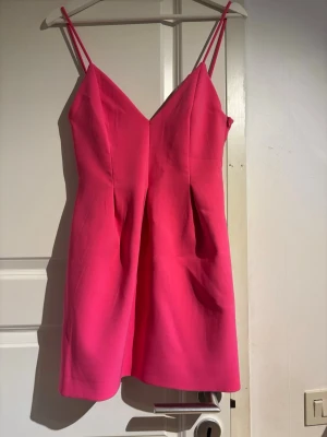 rosa klänning - Snygg kort rosa klänning med smala axelband och v-ringad hals. Klänningen har en enkel, figurnära passform och är perfekt för dig som vill sticka ut. Har aldrig använts därav är lappen kvar! 