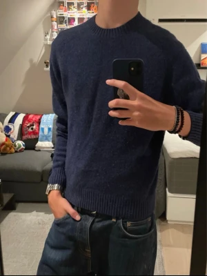 Mörkblå stickad tröja - En enkel och stilren mörkblå stickad tröja med rund halsringning och ribbade muddar vid ärmslut och nederkant. Perfekt att matcha med jeans för en avslappnad look. Materialet är mjukt och bekvämt, och tröjan har en klassisk passform.