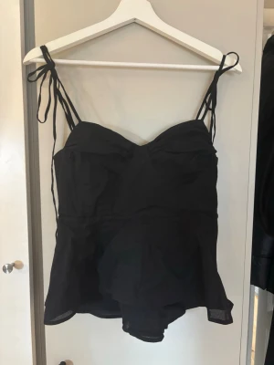 Svart knyt topp  - Superfin svart topp med tunna knytband. Rynkad detalj över bysten och lätt utsvängd nedtill. Perfekt att styla både till jeans och kjol 