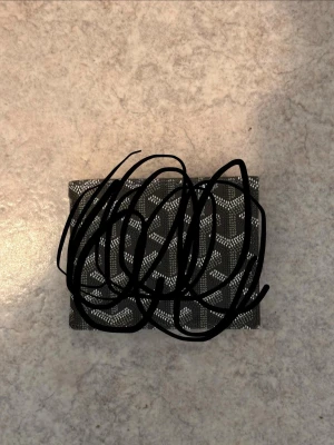 Svart plånbok med mönster - Snygg svart plånbok med vitt grafiskt mönster på utsidan. Plånboken har flera kortfack på insidan och en stilren design. Perfekt storlek för fickan och enkel att ta med sig. Materialet ser ut att vara konstläder.