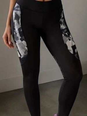 Svarta leggings med mönstrade paneler strl M - Snygga svarta leggings med grafiskt mönstrade paneler i grått och vitt längs sidorna. Hög midja och tight passform som framhäver benen. Perfekta för en sportig och trendig look.
