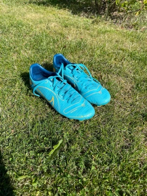 Nike Vapor 14 Academy FG/MG blå - Säljer ett par Nike Vapor 14 Academy FG/MG fotbollsskor i en snygg blå färg med gula detaljer. Skorna har snörning och är designade för spel på både natur- och konstgräs. Lätta och smidiga med bra grepp för snabba rörelser på planen.