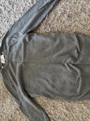 Grå rundhalsad stickad tröja - En enkel och stilren grå stickad tröja med rund halsringning. Lätt och matcha outfits med denna tröja. Även varm skön och väldigt snygg.