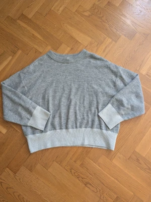 Grå oversized stickad tröja - Mysig grå stickad tröja med breda ribbade muddar vid ärmslut och nederkant. Tröjan har en avslappnad, oversized passform och rund halsringning. Perfekt för lager på lager och chill dagar. Materialet känns mjukt och skönt mot huden.