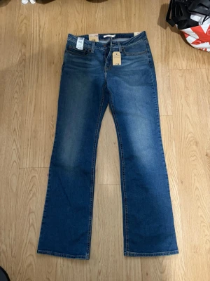 Blå bootcut jeans med etikett - Säljer ett par levis blå bootcut jeans med snygg tvätt och raka ben. Jeansen har fem fickor och hällor för bälte. Perfekta för dig som gillar en tidlös och avslappnad stil. Materialet är denim i bomull.