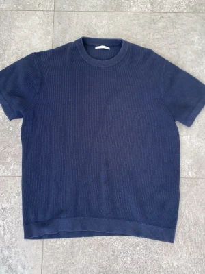 Mörkblå stickad tröja - En stilren mörkblå ribbad topp med korta ärmar och rund hals. Lite varmare t shirt och är inte använd jätte många gånger. Hör av er vid frågor✅