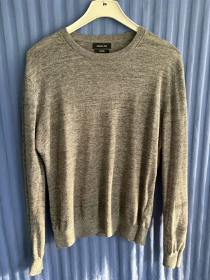 Grå stickad tröja från Massimo Dutti - Snygg grå stickad tröja från Massimo Dutti i 100% linne. Tröjan har rund halsringning, långa ärmar och ribbade muddar vid ärmslut och nederkant. Perfekt basplagg för en stilren och enkel look.