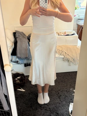 Ljusbeige långkjol i satin - Säljer en stilren ljusbeige långkjol i satin med lätt utsvängd passform. Kjolen har en slät midja och stängs med dragkedja i sidan. Perfekt för dig som gillar en enkel men elegant look.