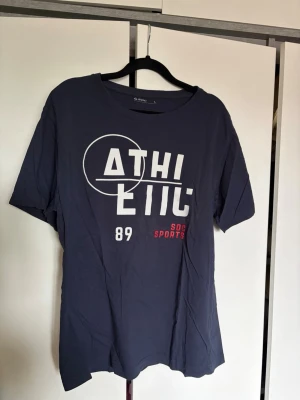 Mörkblå t-shirt från SOC - Mörkblå t-shirt från SOC med vit och röd text på bröstet där det står 'ATHLETIC 89 SOC SPORTS'. 