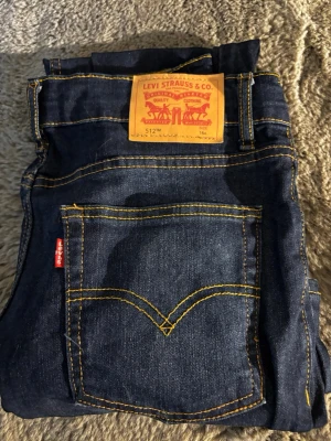 Levi's 512 Slim Taper jeans mörkblå - Säljer ett par Levi's 512 Slim Taper jeans i mörkblå denim med klassiska gula sömmar och femficksmodell. Jeansen har en smalare passform som smalnar av nedtill och är tillverkade i bomull. Perfekta för dig som gillar en clean och tidlös look.