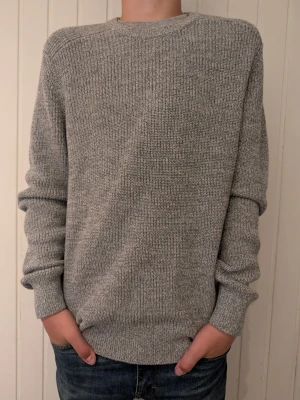 Grå Gap stickad tröja i bomull - En enkel och stilren grå stickad tröja från Gap med rund hals och långa ärmar. Tröjan har ribbstickade muddar vid ärmslut och nederkant. Perfekt för lager på lager och passar till det mesta i garderoben.