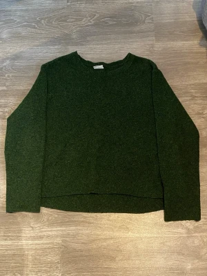 Mörkgrön stickad tröja - En enkel och stilren mörkgrön stickad tröja med rund hals och långa ärmar. Tröjan har en rak passform och är gjord i ett mjukt, mysigt material som passar perfekt till kyligare dagar. 