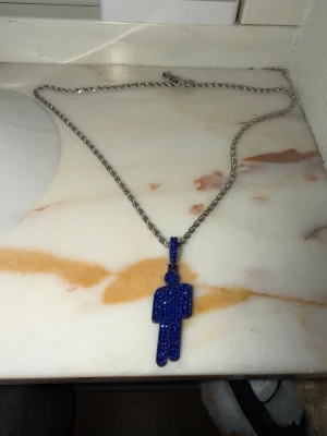Silverfärgat halsband med blå blohsh - Säljer ett silverfärgat halsband med en unik blå berlock i form av en blohsh. Berlocken är täckt av små blå stenar som ger ett glittrande intryck. Kedjan är tunn och vriden, vilket ger ett modernt och trendigt utseende. Halsbandet är 55 cm långt och aldrig använt <3 