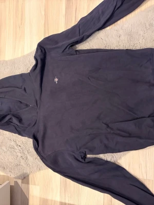Mörkblå hoodie från GANT - Snygg mörkblå hoodie från GANT med liten broderad logga på bröstet. Klassisk modell med huva och långa ärmar. Tillverkad i mjukt bomullsmaterial som känns skönt mot huden. Perfekt för en avslappnad och stilren look.