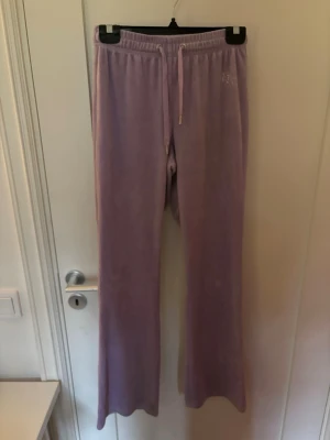 Ljuslila mjukisbyxor i velour - Säljer ett par ljuslila mjukisbyxor i mjuk velour med raka ben och dragsko i midjan. Byxorna har en avslappnad passform och resår i midjan för extra komfort. Perfekta för chill dagar hemma eller när du vill vara extra bekväm.