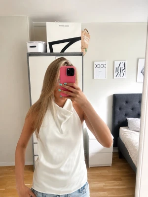 Vit satintopp  - Krämvit topp i satin och med öppen rygg. Den har hög krage som man knäpper runt halsen. Aldrig använd. 