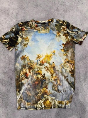 T-shirt med konsttryck från Criminal Damage - Unik t-shirt från Criminal Damage med ett detaljerat konsttryck som täcker hela plagget. T-shirten har rund hals, korta ärmar och är tillverkad i mjuk bomull. Perfekt för dig som vill sticka ut med en kreativ och färgstark stil.