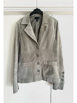 Grå / grågrön kavaj i 100% äkta mocka - storlek 40 - H&M - Stilren grå / grågrön jacka / kavaj i 100% äkta skinn / mocka från H&M i storlek 40. Tidlös modell med klassisk krage, knäppning framtill och diskreta fickor. Dekorativa knappar knappar vid ärmsluten och fin rynkad resår baktill i midjan. En tidlös klassiker som kommer hålla säsong efter säsong. Mycket gott skick, som ny!
