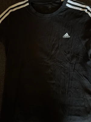Svart Adidas t-shirt med vita ränder - Svart Adidas t-shirt  Vita ränder på axlarna och broderad Adidas-logga på bröstet.