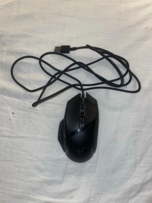 Svart gamingmus från Razer - Säljer en svart gamingmus från Razer med ergonomisk form och flera programmerbara knappar. Musen har USB-anslutning med flätad kabel och är tillverkad i plast med gummerade sidor för bättre grepp. Perfekt för gaming och snabba rörelser.