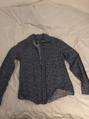 Blommig skjorta från Dressmann - Snygg långärmad skjorta från Dressmann med blommigt mönster i blått och vitt. Skjortan har klassisk krage och knappar framtill. Perfekt för dig som vill sticka ut lite extra med en cool och unik stil. Pris går att diskutera!!!!✅🙌