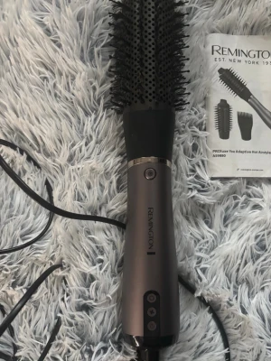 Remington varmluftsborste med tillbehör - Säljer en Remington PROluxe varmluftsborste i svart och grått. Medföljer flera utbytbara borsthuvuden och stylingmunstycke. Perfekt för att skapa volym, lockar eller släta frisyrer. Ergonomiskt handtag och enkel knappstyrning. Sladd för elanslutning.