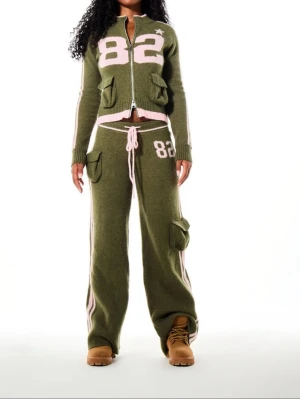 Grönt loungewear-set med stjärnor, Strl M - Oanvändt set med prislappar kvar! Både tröjan & byxorna är i Strl M.  Mysigt loungewear-set i olivgrönt med ljusrosa detaljer. Setet består av en ziptröja och byxor med breda ben, båda med stickade siffror och stjärnor. Flera fickor med lock och kontrastfärgade ränder längs ärmar och ben. Perfekt för chill dagar hemma.