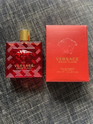 Versace Eros Flame Eau de Parfum - Versace Eros Flame Eau de Parfum i en lyxig röd glasflaska med guldfärgat lock och Medusa-huvud i relief. Flaskan rymmer 100 ml och kommer med matchande röd kartong med gulddetaljer. En elegant och intensiv doft för dig som gillar exklusiva parfymer.