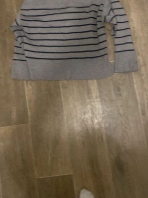 Grå tröja med marinblå ränder - Säljer en stilren grå tröja med marinblå horisontella ränder. Tröjan har en rak passform och långa ärmar. Perfekt för en avslappnad och trendig look.