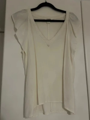 Vit blus med volangärmar - Snygg vit blus med v-ringning och volangdetaljer vid ärmarna. I tyget vid V-et går en tråd lite upp men inget som syns tydligt. Fläckfri och perfekt till sommaren!