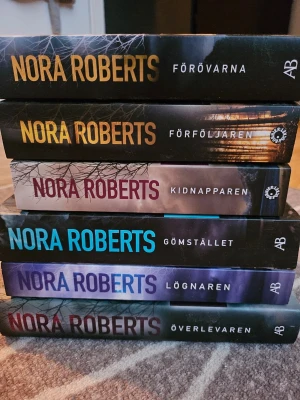 Nora Roberts spänningsromaner, 6 st - Säljer ett bokpaket med sex spänningsromaner av Nora Roberts: Förövarna, Förföljaren, Kidnapparen, Gömstället, Lögneren och Överlevaren. Böckerna har färgstarka omslag i svart, blått, gult och lila och är i pocketformat. Perfekt för dig som gillar nervkittlande läsning!